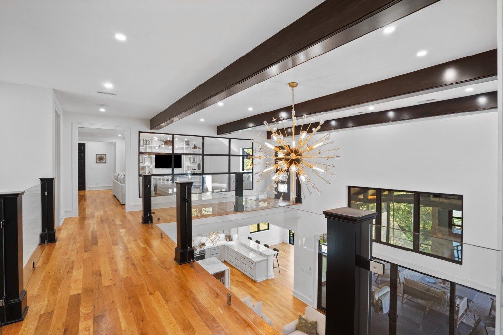 Upper-level overlook with exposed wood beams, sputnik chandelier, and glass rails
